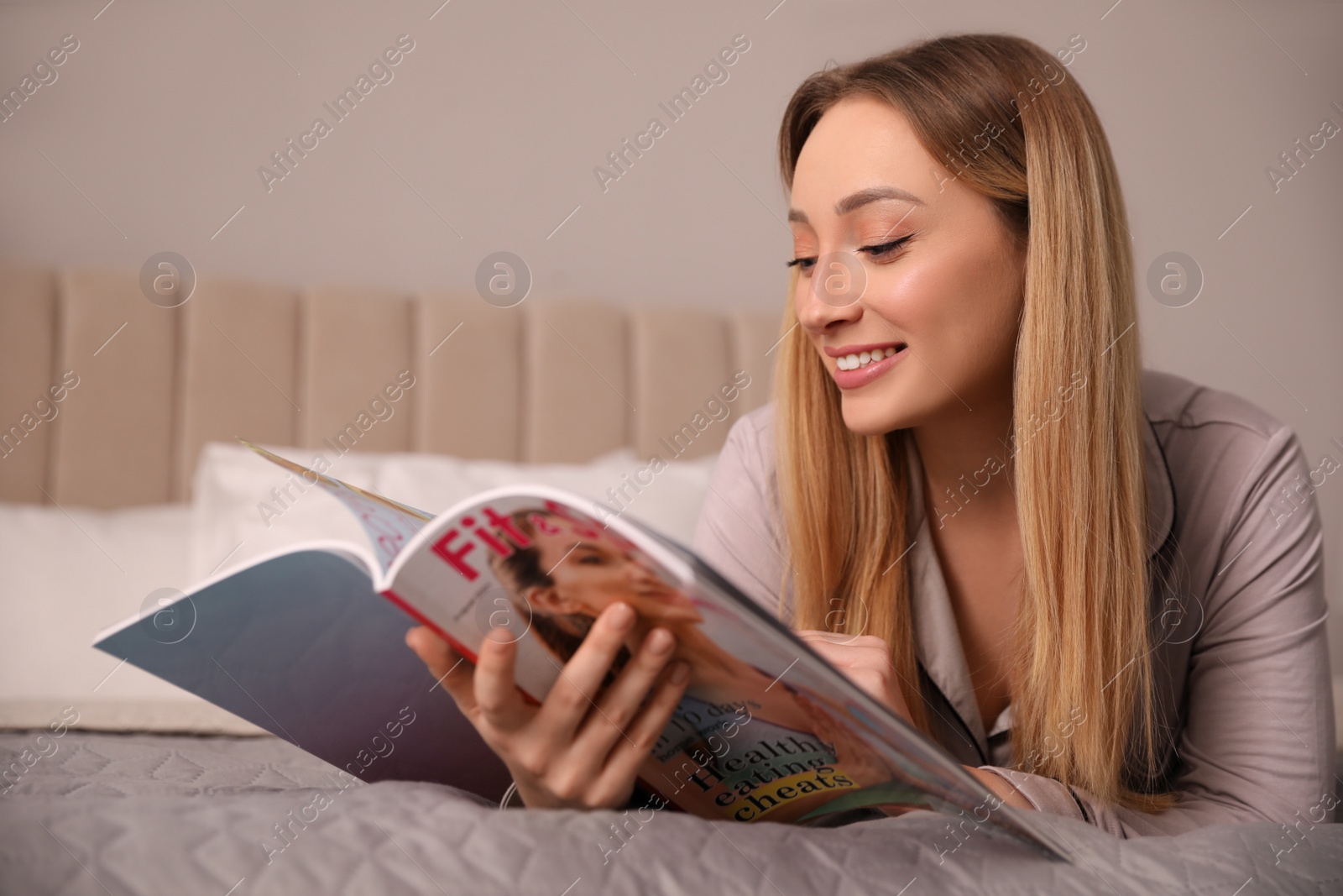 Photo of Happy woman reading magazine on bed indoors