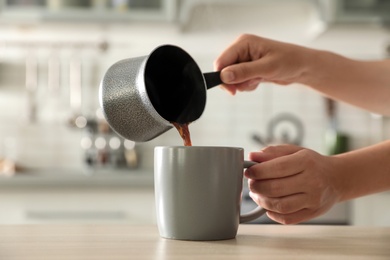 Photo of Woman pouring fresh coffee into cup at table in kitchen, closeup