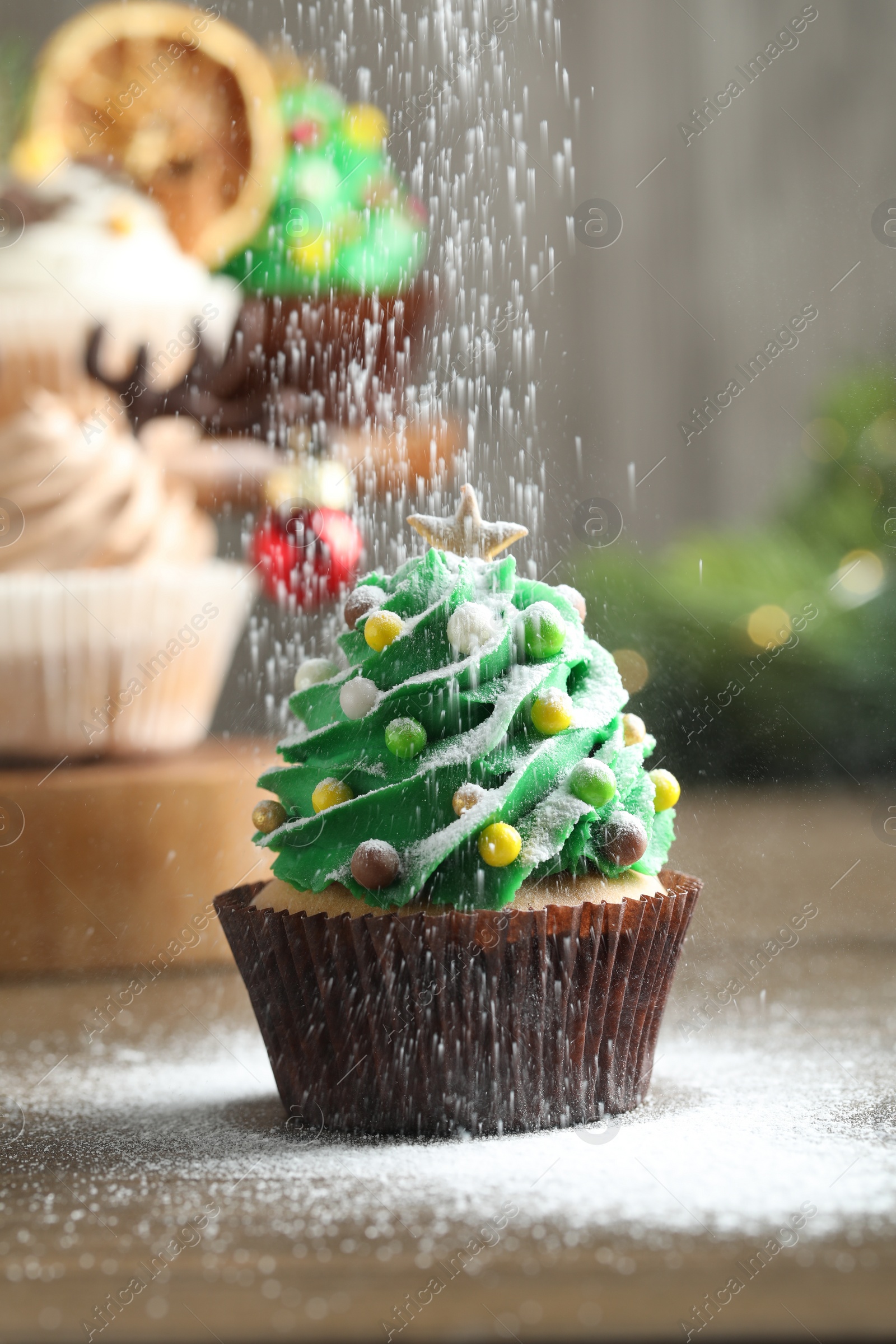 Photo of Sprinkling powdered sugar on Christmas tree shaped cupcake at wooden table