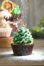 Photo of Sprinkling powdered sugar on Christmas tree shaped cupcake at wooden table