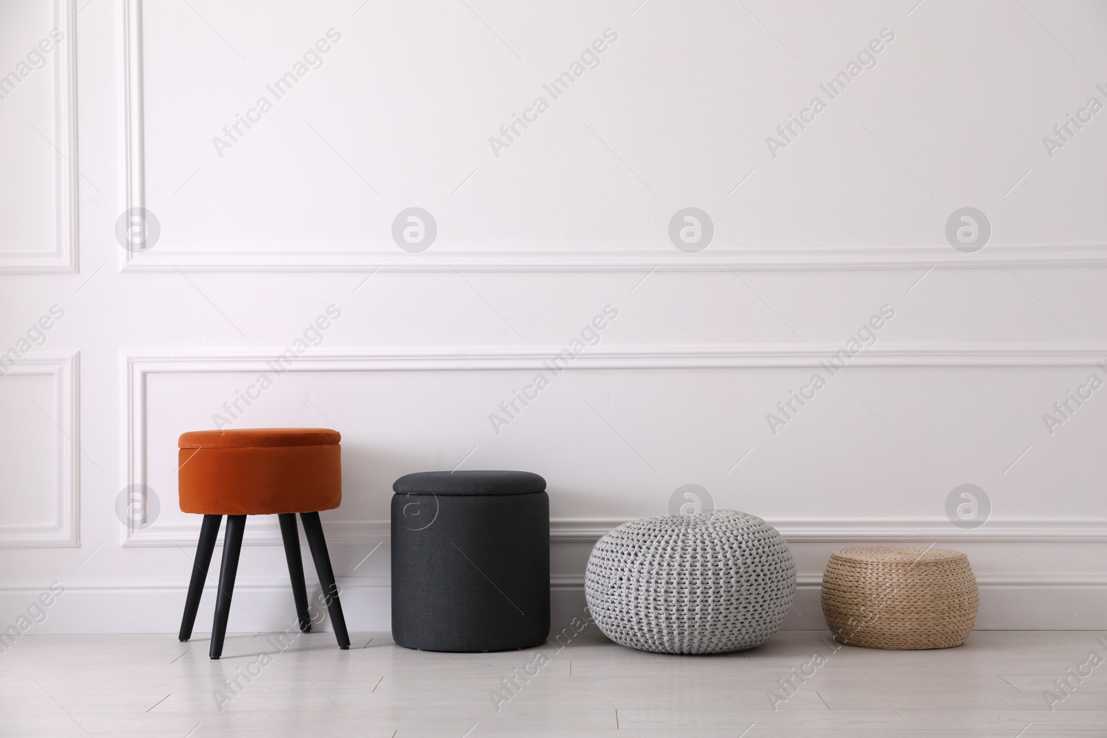 Photo of Different stylish poufs and ottomans near light wall