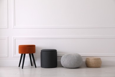 Different stylish poufs and ottomans near light wall