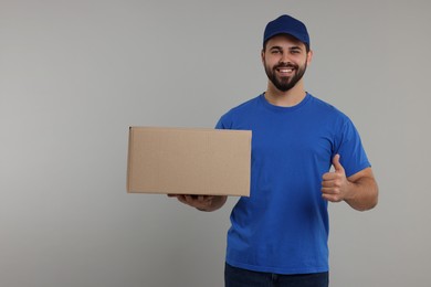 Photo of Happy courier with parcels showing thumb up on grey background, space for text