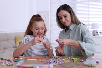 Photo of Happy mother with her daughter making beaded jewelry at home