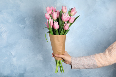 Woman with beautiful pink spring tulips on light blue background, closeup