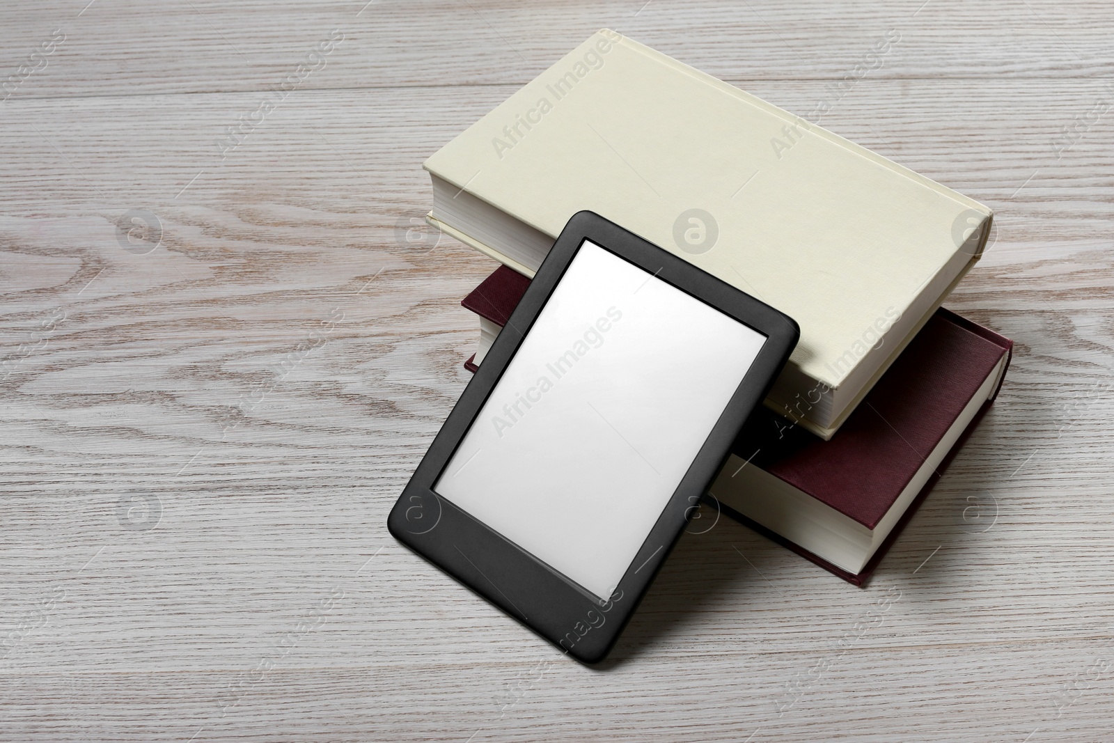 Photo of Portable e-book reader and hardcover books on white wooden table