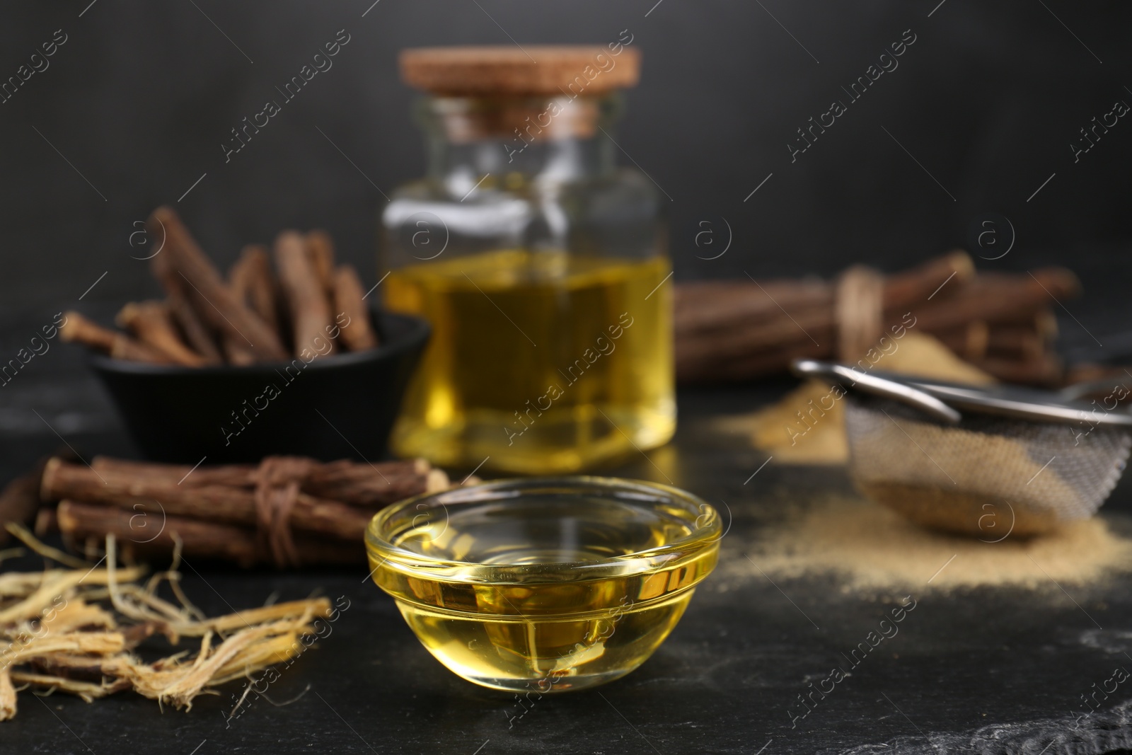 Photo of Bowl with essential oil and dried sticks of liquorice root on black table. Space for text