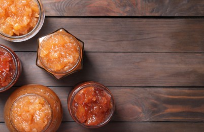 Photo of Delicious apple jam in jars on wooden table, flat lay. Space for text