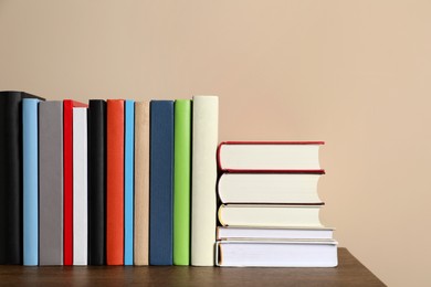 Photo of Many different hardcover books on wooden table near beige wall. Space for text