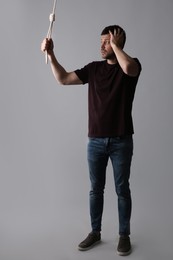 Depressed man with rope noose on light grey background