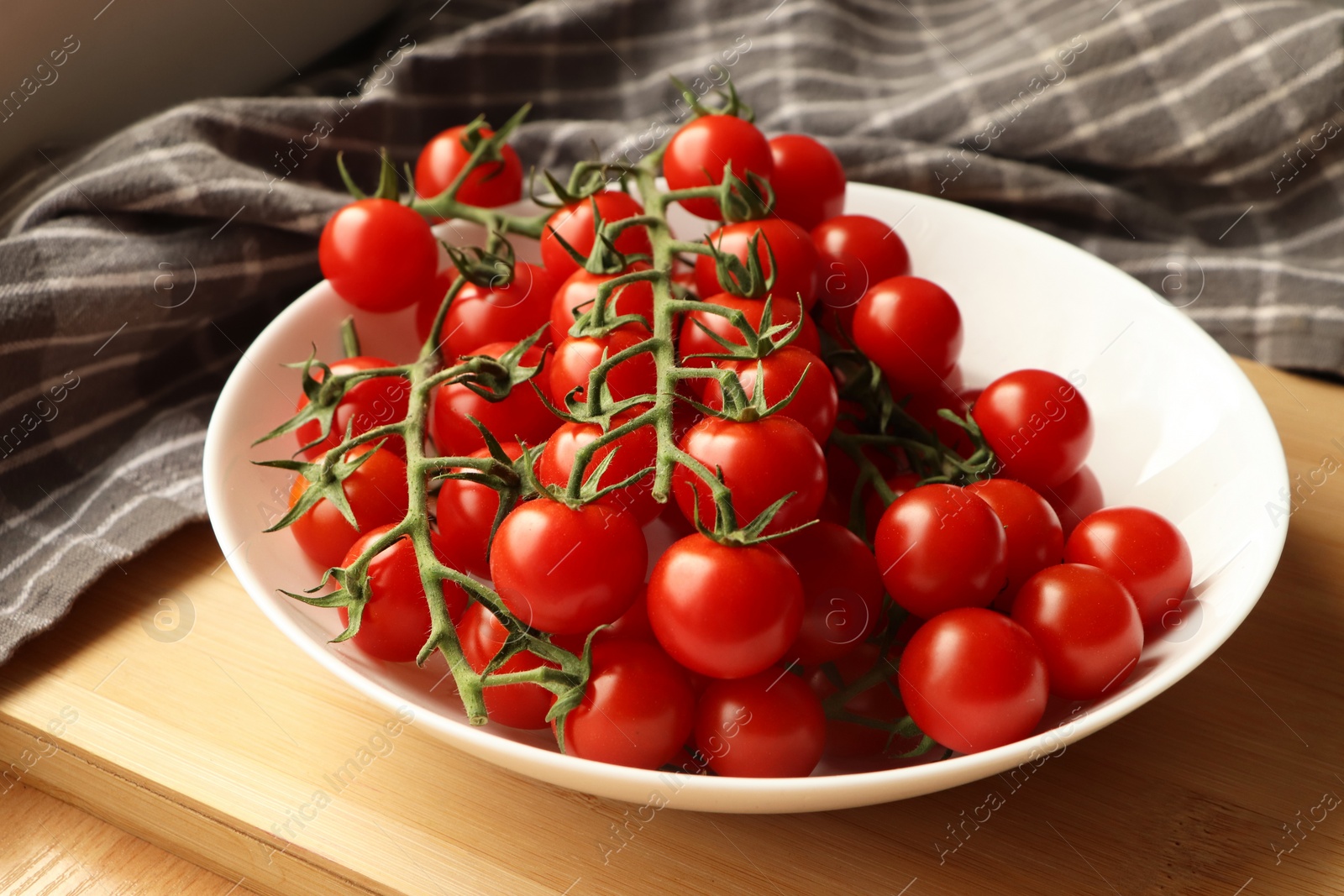 Photo of Plate of ripe whole cherry tomatoes on wooden table, closeup