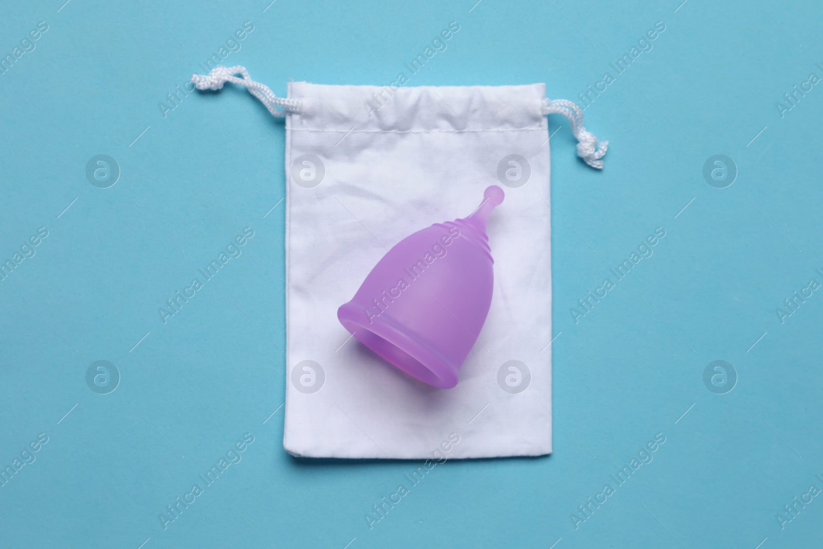 Photo of Menstrual cup with cotton bag on light blue background, top view. Reusable feminine hygiene product