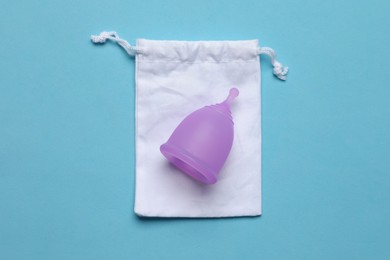 Menstrual cup with cotton bag on light blue background, top view. Reusable feminine hygiene product