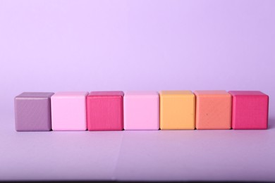 Photo of Empty colorful cubes on lilac background, space for design