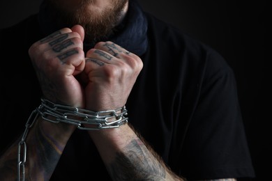 Photo of Man with chained hands on dark background, closeup. Hostage