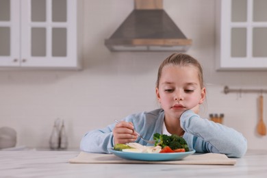Photo of Cute little girl refusing to eat dinner in kitchen, space for text