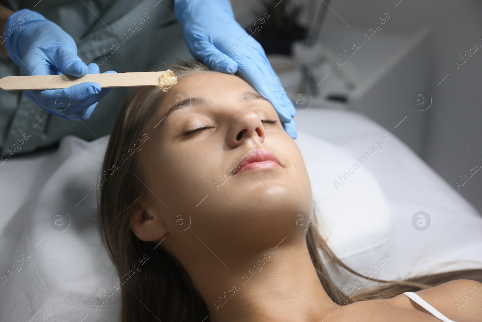 Photo of Young woman undergoing hair removal procedure on face with sugaring paste in salon