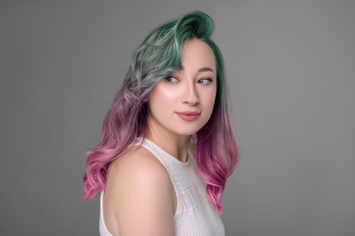 Trendy hairstyle. Young woman with colorful dyed hair on grey background