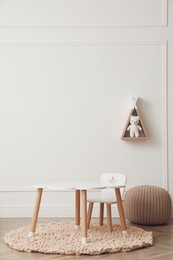 Photo of Cute child room interior with furniture, toy and wigwam shaped shelf on white wall