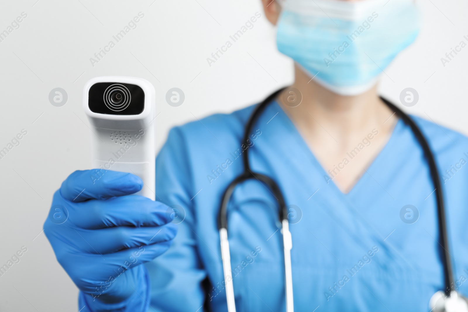 Photo of Doctor with infrared thermometer on light background, closeup. Checking temperature during Covid-19 pandemic