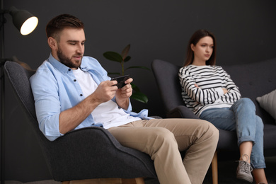 Young man preferring smartphone over his girlfriend at home. Relationship problems