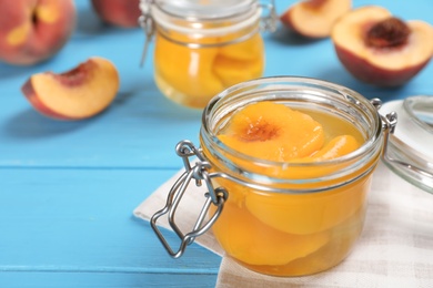 Glass jar with conserved peach halves on wooden table. Space for text