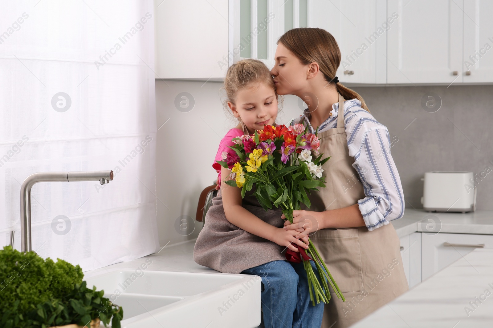 Photo of Little daughter congratulating mom with bouquet of flowers in kitchen. Happy Mother's Day