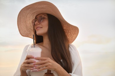 Photo of Beautiful young woman with tasty milk shake outdoors, space for text