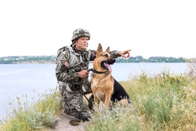 Photo of Man in military uniform with German shepherd dog near river