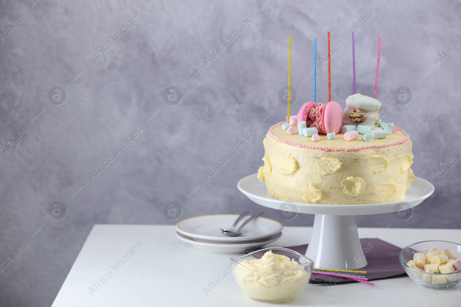 Photo of Delicious cake decorated with macarons, marshmallows and candles served on white table against grey background, space for text