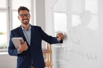 Photo of Happy teacher with book explaining mathematics at whiteboard in classroom