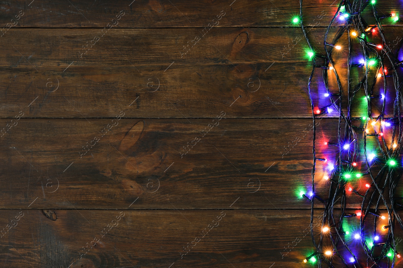 Photo of Glowing Christmas lights on brown wooden background, top view. Space for text