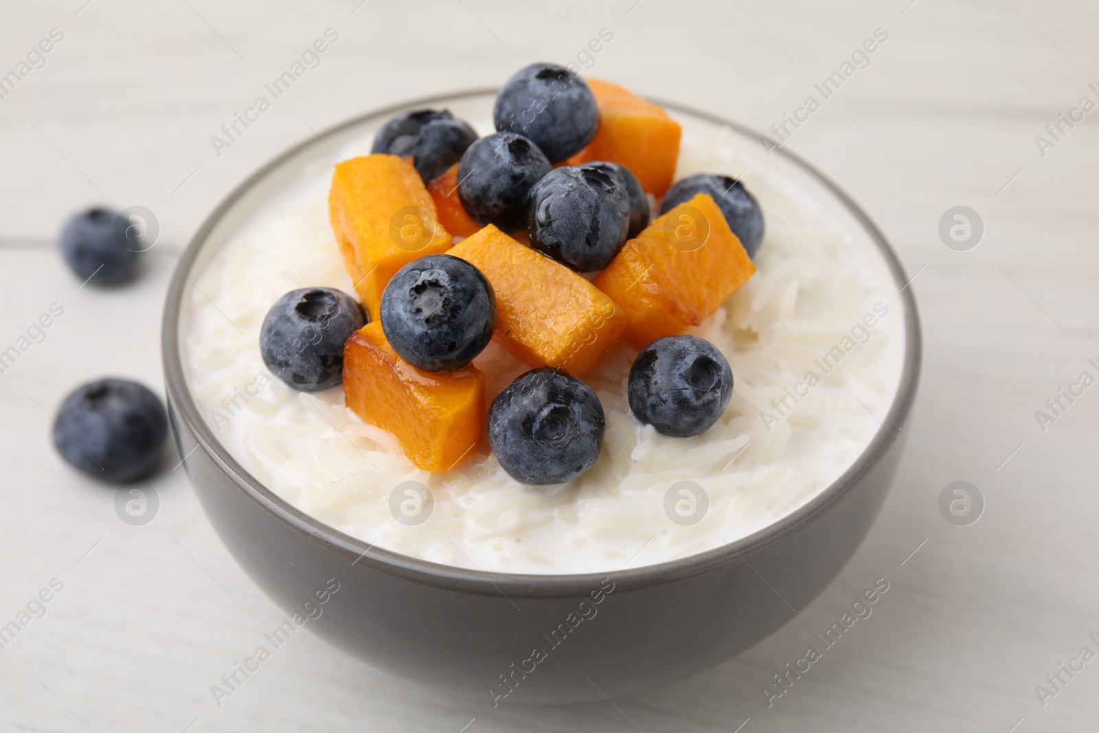 Photo of Bowl of delicious rice porridge with blueberries and pumpkin on white table, closeup