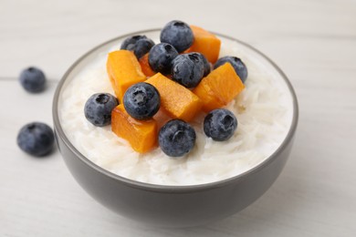 Photo of Bowl of delicious rice porridge with blueberries and pumpkin on white table, closeup