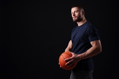 Photo of Athletic young man with basketball ball on black background. Space for text