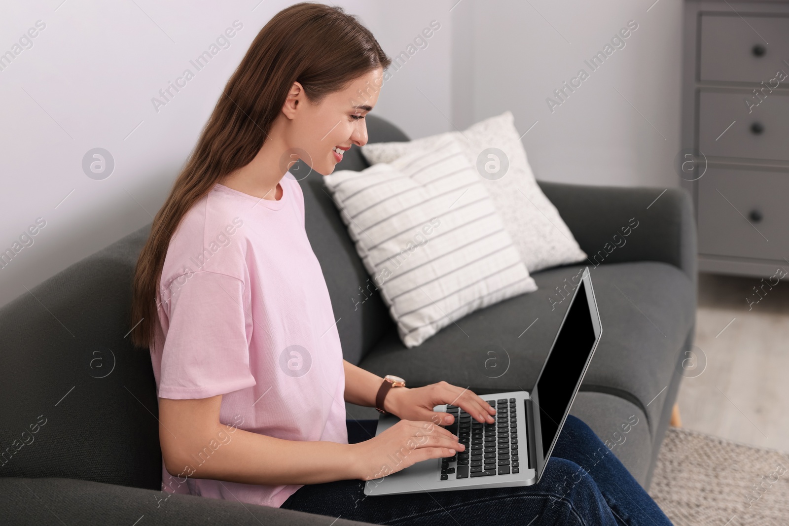 Photo of Happy young woman with laptop on sofa at home