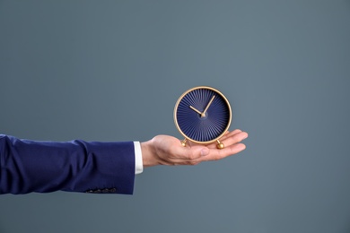 Young businessman holding clock on color background. Time management