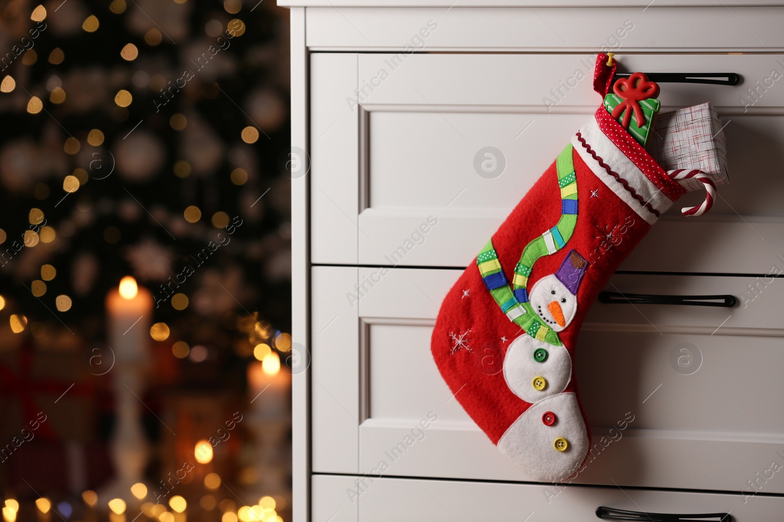 Photo of Stocking with sweets and gift hanging on chest of drawers in room, space for text. Saint Nicholas Day