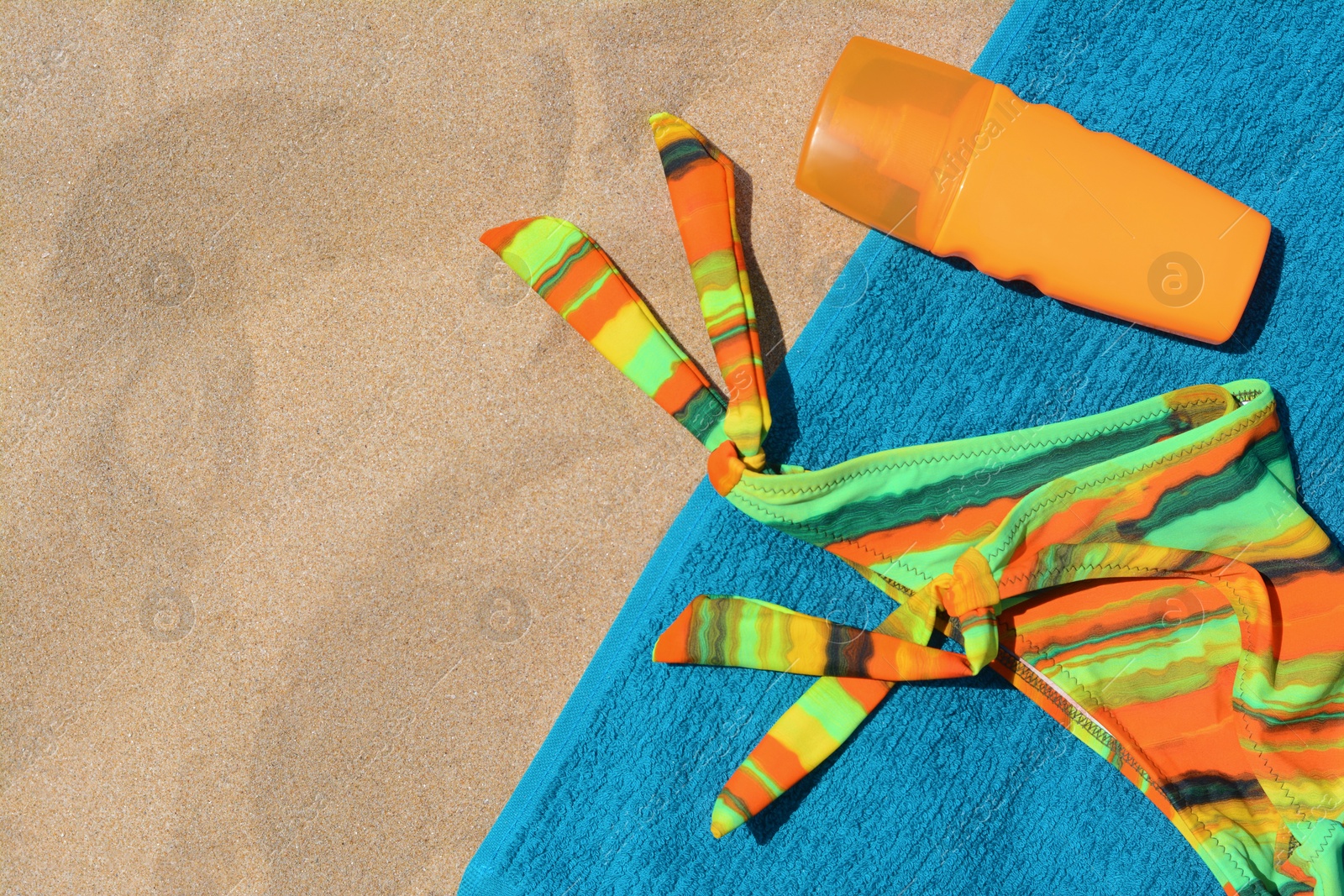 Photo of Soft blue beach towel with bottle of sunscreen and colorful bikini bottom, flat lay. Space for text