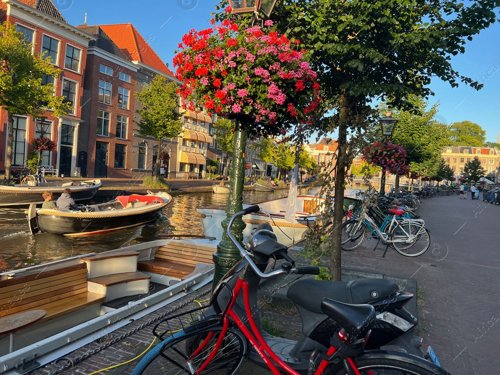 Photo of Leiden, Netherlands - August 1, 2022: Picturesque view of city canal with moored boats and parked bicycles