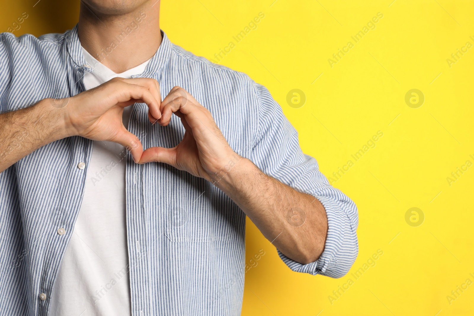 Photo of Man making heart with hands on yellow background, closeup. Space for text