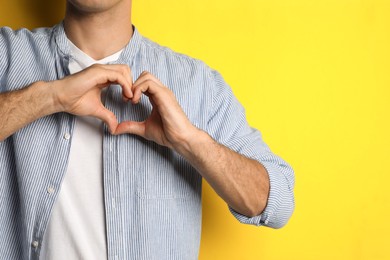 Photo of Man making heart with hands on yellow background, closeup. Space for text