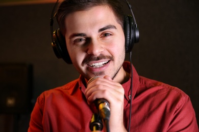 Young singer with microphone recording song in studio