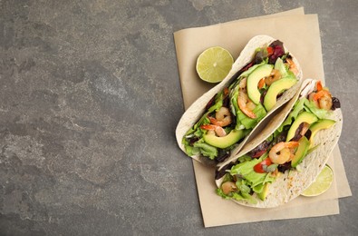 Delicious tacos with shrimps, avocado and lime on grey table, top view. Space for text