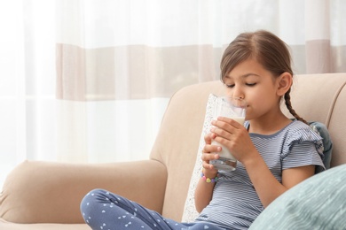 Photo of Cute little girl drinking milk on sofa at home