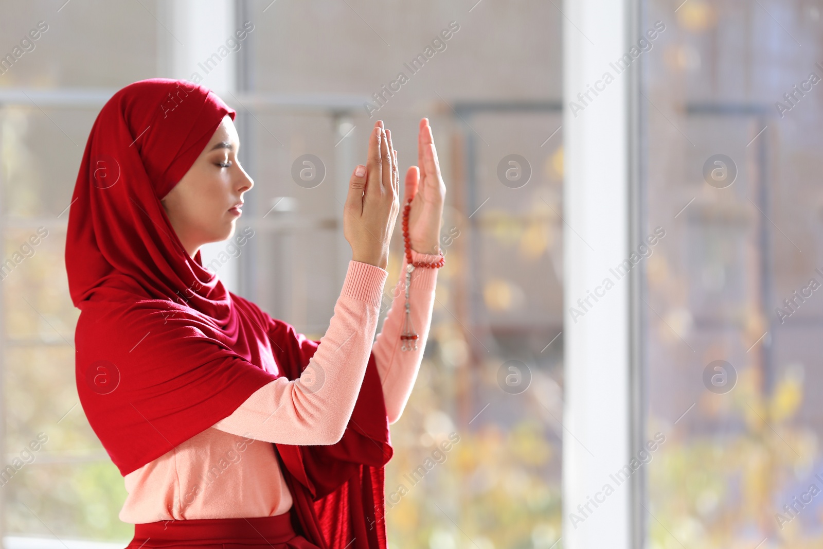 Photo of Young Muslim woman in hijab praying indoors. Space for text