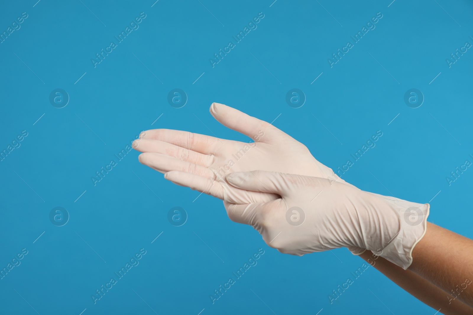 Photo of Doctor wearing medical gloves on light blue background, closeup