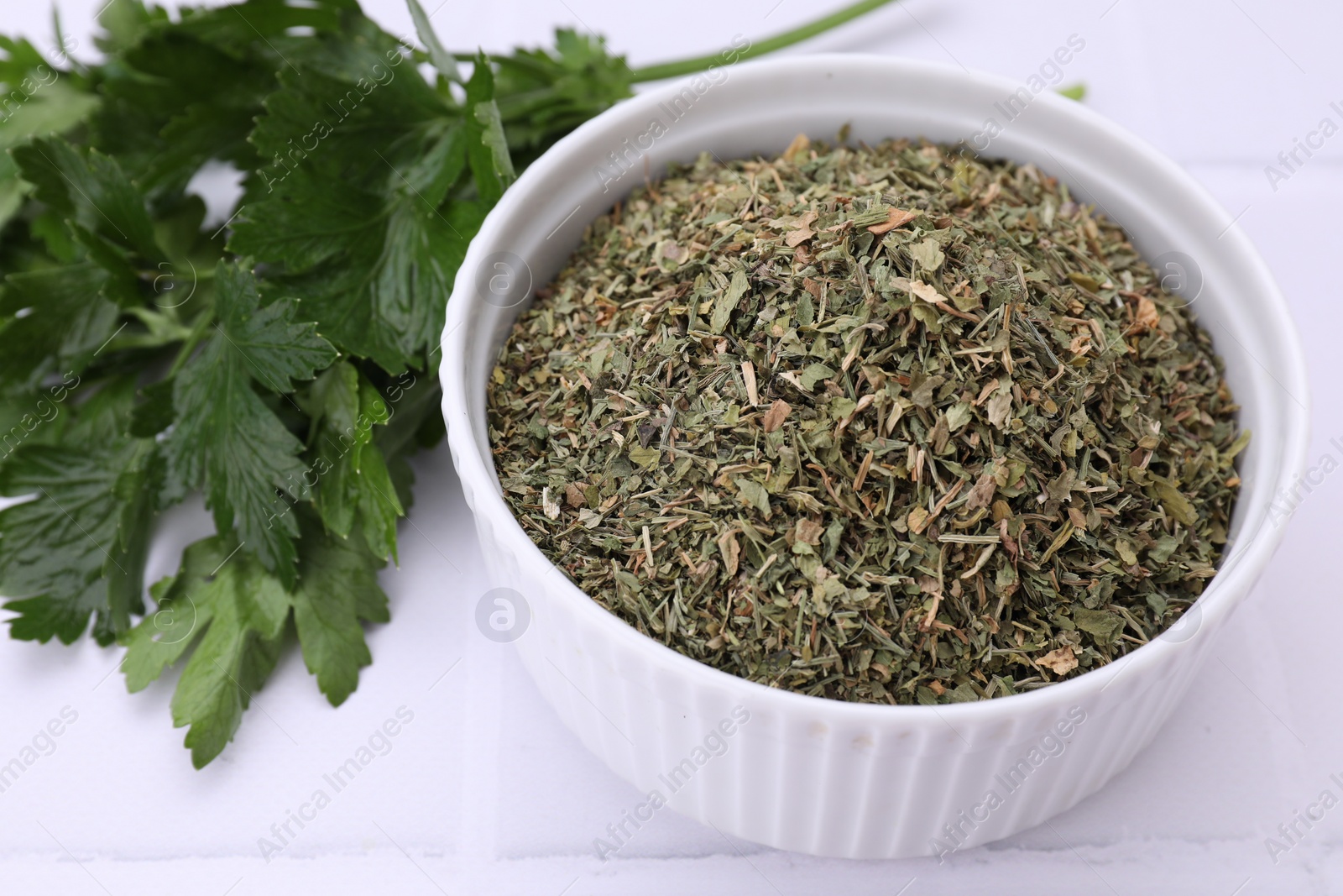 Photo of Dried parsley and fresh leaves on white table, closeup