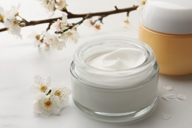 Jars of face cream and flowers on white marble table