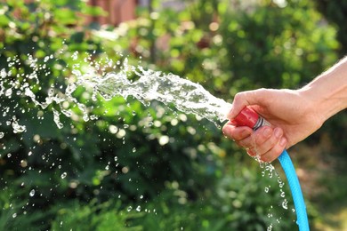 Photo of Man pouring water from hose in garden, closeup